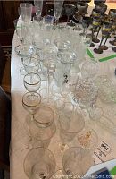 Various clear and gold-rimed glassware including wine, sundae, shot, Irish coffee, and highball glasses displayed on a table with cut glass bowls and butter tray.