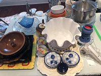 Wide view of assorted kitchenware items showing bowls, platters, ice bucket, ramekins, teapot, garlic press, and metal pots.