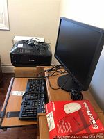 Desk with Canon MX512 printer on wooden stand, Samsung 21-inch monitor, two Microsoft wired keyboards and Microsoft Basic Optical mouse in red and white box on desk. Power cables and cords are loosely placed on devices.