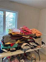 Stack of assorted fabrics and blankets on a table near a window.