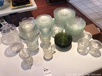 Overview of the full lot showing all glassware pieces on table including decanter, cups, bowls, plates, green bowl, and canister.