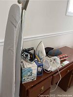 Photo showing multiple irons, ironing board and cushions on wood furniture surface.