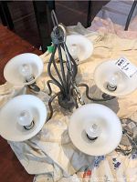 Image of the hanging light fixture flat on the floor showing the five frosted glass shades and metal frame with light bulbs installed.