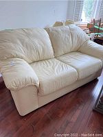 Front view of cream leather-like loveseat showing two seat cushions and puffy armrests.