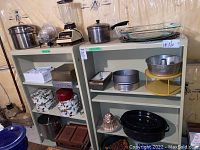 Two matching beige metal shelving units with various kitchen and storage items on the shelves. Showing general wear and located in basement.
