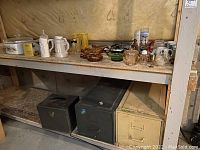 Shelf in basement with metal drawers beneath and various mugs, glass bowls, and decorative items on top.