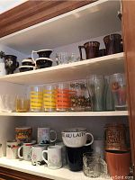 Three shelves of various mugs, glasses, and kitchenware items shown to display the lot's content.