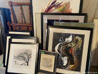 Wooden single bed headboard and footboard leaning on wall alongside several framed pictures and a mirror; shows several framed art pieces and the wooden headboard and footboard with some wear.