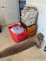 Overall view of assorted patterns in clear bins and storage shelves, red bin of fabrics and rolled fabric on floor