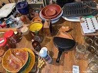 Overview of wooden bowls, ceramic plates with autumn leaf design, a black grill pan, blue ceramic pot, and assorted small containers on table