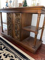 Full angled view of the wooden sideboard showing the carved door, open shelves, and top surface with some display decor visible.