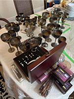 Full view of silver plated goblets, trays, napkin rings, gravy boat, creamer, and corkscrew set on table