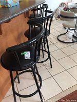 Four black metal stools with vinyl seat cushions under counter, one seat cushion has a tear.