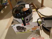 T-fal ActiFry air fryer on its original box, black with clear lid and control button on top.