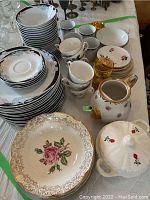 Full view of the china set including plates, bowls, cups, teapot, covered bowl, and glass on a table