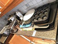 Photo showing toaster, pots with lids, utensil caddy, cutting boards, and trays on kitchen counter.