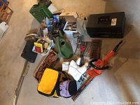 Overall lot showing trimmer, skates, coolers, toolbox, watering can, painting supplies, and screwdriver set on concrete floor.