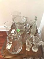 Photo showing various clear glass vases of different shapes and sizes on a wooden table.
