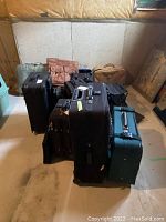 Overview of vintage suitcases arranged on basement floor showing various colors and materials, including leather and hard-shell cases.
