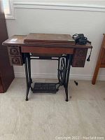 Front view of vintage wooden table with manual Singer sewing machine on top and power adapter to the right. Table has four drawers and cast iron treadle base.