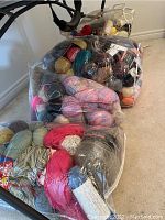 Four transparent bags filled with assorted yarns in various colors and textures placed on carpeted floor.