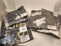 7 NHL T-shirts packaged and folded, black color predominates, showing Philadelphia Flyers and Arizona Coyotes logos