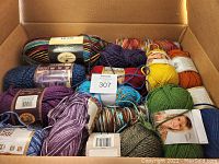 Photo showing a box filled with various yarn skeins of different colors and brands including Rainbow Classic and Vanna White.
