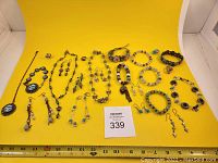 Full lot overview including necklaces, bracelets, earrings, and rings arranged on yellow background with measuring tape showing sizes.