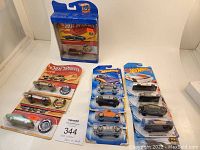Photo showing the full assortment of 14 Hot Wheels cars in original packaging laid out on a white surface, including two anniversary edition cards and others blank cards.