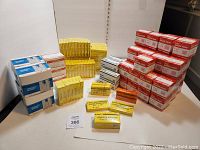 Photo of multiple boxes of medical bandages and supplies arranged on a table, including yellow, red, blue and orange boxes, showing new unopened packaging.