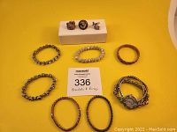 Photo showing entire lot: one watch, three rings, and six bracelets arranged on yellow backdrop with lot number card visible.