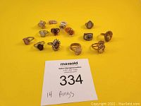 Overview of 14 various rings arranged on yellow background showing different sizes and designs