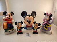 View of all five coin banks in lot including large Mickey Mouse head, Minnie Mouse seated bank, Mickey Mouse drum major bank, and two small Mickey tuxedo banks.