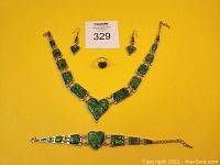 Full view of 5-piece paua shell jewelry set on yellow background including choker necklace, bracelet, ring and earrings.