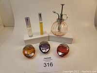 Perfume bottles displayed on white stands and table, showing 3 BVLGARI Omnia perfumes, 2 smaller perfume sprays, and an empty pink glass perfume mister bottle with silver spray pump.