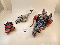 Photo showing Optimus Prime in robot mode, Scorponok in helicopter form, and a smaller red vehicle figure on a white surface.