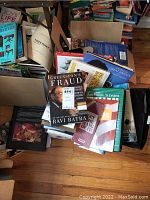 Photo of assorted stacked books including 'Greenspan's Fraud,' 'Just Listen 'n Learn,' and other titles relating to reference, biography, and home.