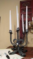 Full view of the metal fleur de lis style candelabra holding four white taper candles.