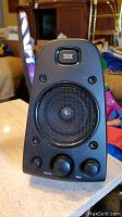 Front view of Logitech speaker showing THX badge, speaker mesh, volume and bass control knobs.