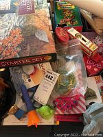 Photo showing assorted crafting supplies such as string, ribbons, children's toys, and boxes of games and kits in a pile.