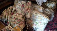 Floral patterned chair pads and cushions, piled and wrapped in plastic bags, showing different floral designs and colors.