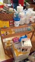 Photo of assorted medical and first aid supplies on a wooden shelf including lotions, gloves, bandages, tapes, and two boxed steam inhalers on the floor beneath.