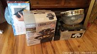 Lot items including boxed Homedics Envirascape waterfall fountain, boxed vent covers, boxed dome light, and chrome 3-head ceiling light fixture on wooden floor.