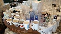 Full view of mugs and drinking glasses arranged on a table, showing variety of ceramic mugs and different types of drinking glasses