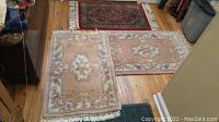 Set of 3 rugs on wooden floor, two matching pink floral handmade wool Oriental rugs with fringe, and one red Oriental rug