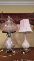 Pair of table lamps on a surface, one with a glass shade and patterned glass base, the other with a fabric shade and opaque white base