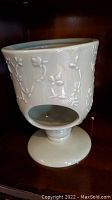 White porcelain tea steeper with floral relief design on a pedestal base, open bottom for warming with flame