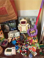 Photo showing assortment of vintage and modern toys and games including robot toy, Koosh ball scoop, CSI game, and small toys.