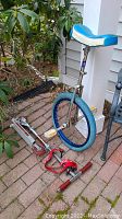 Side view of unicycles and scooter together, showing unicycle seated on ground and scooter laying nearby.