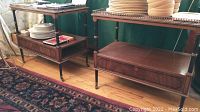 Pair of vintage solid wood side tables with metal slide guards and casters placed on wooden floor with a patterned rug nearby.